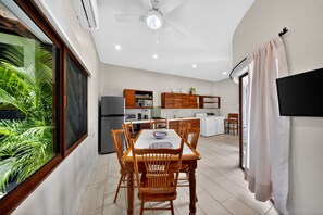 A modern kitchen with a dining area, a ceiling fan, and a large window with a view of greenery. - Hidden Garden Oasis - Ground Floor + Pool (Lo de Marcos)