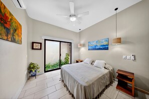 A bedroom with a bed, a ceiling fan, a window with a view, a bedside table, and a wall-mounted light fixture. - Hidden Garden Oasis - Ground Floor + Pool (Lo de Marcos)