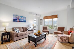 Een woonkamer met een bank, fauteuils, een salontafel, een vloerkleed, een schilderij en een raam met uitzicht.