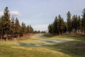 A golf course with a clear path, surrounded by tall pine trees. - 2BR | Pool, Hot Tub, Golf, UBC & Airport (Kelowna)