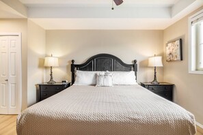 Een slaapkamer met een groot bed, twee nachtkastjes met lampen, een deur en een schilderij aan de muur.