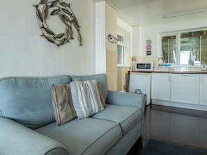 A living room with a sofa, a decorative wall piece, and a kitchen area with cabinets and a microwave. - Smugglers View by Interhome (Mevagissey)