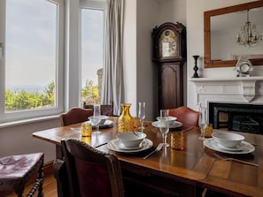 A dining room with a table set for four, a grandfather clock, and a fireplace. - Smugglers View by Interhome (Mevagissey)