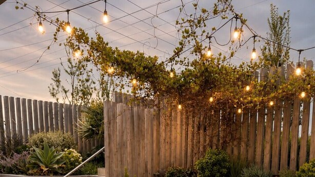 Eine Holzterrasse mit Tisch und Stühlen, eine Treppe und ein Holzzaun mit Kletterpflanzen.