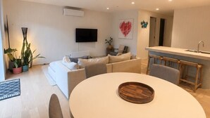 Ein modernes Wohnzimmer mit einem runden Esstisch, einer Couch, einem Fernseher und einer Küchenzeile.