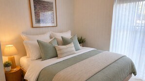 Ein ordentlich bezogenes Bett mit Grün-Weiß-Farbschema, eine Nachttischlampe und ein gerahmtes Bild an der Wand.