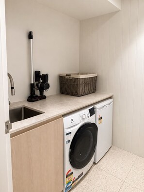 Un espace buanderie compact comprenant un lave-linge, un évier et un étendoir.