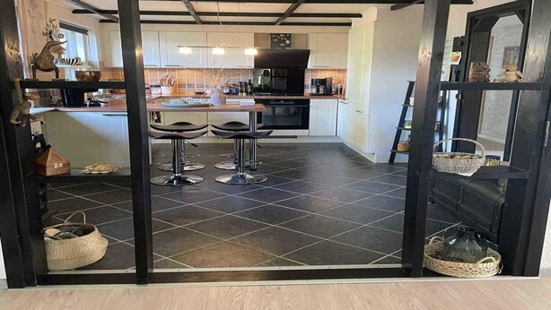 A modern kitchen with dark tiles, a central island, and bar stools.