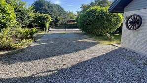 A gravel driveway leading to a white building with a large wheel on the wall.