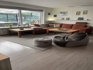 Ein modernes Wohnzimmer mit Sofa, Couchtisch und Sitzsack, ein großes Fenster mit Blick und eine Wand mit gerahmten Bildern.