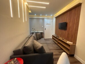 Ein modernes Wohnzimmer mit einer Couch, einem Flachbildfernseher an einer Holzvertäfelung und eingelassener Beleuchtung.