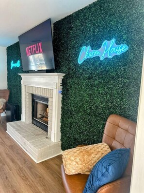 Un salon avec une cheminée, un téléviseur et un panneau lumineux au néon.