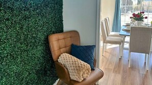 A room with a green wall, a neon sign reading 'Charm House,' a brown leather chair with a blue pillow, and a dining area with a chandelier. - Summerville’s Charm House (Summerville)