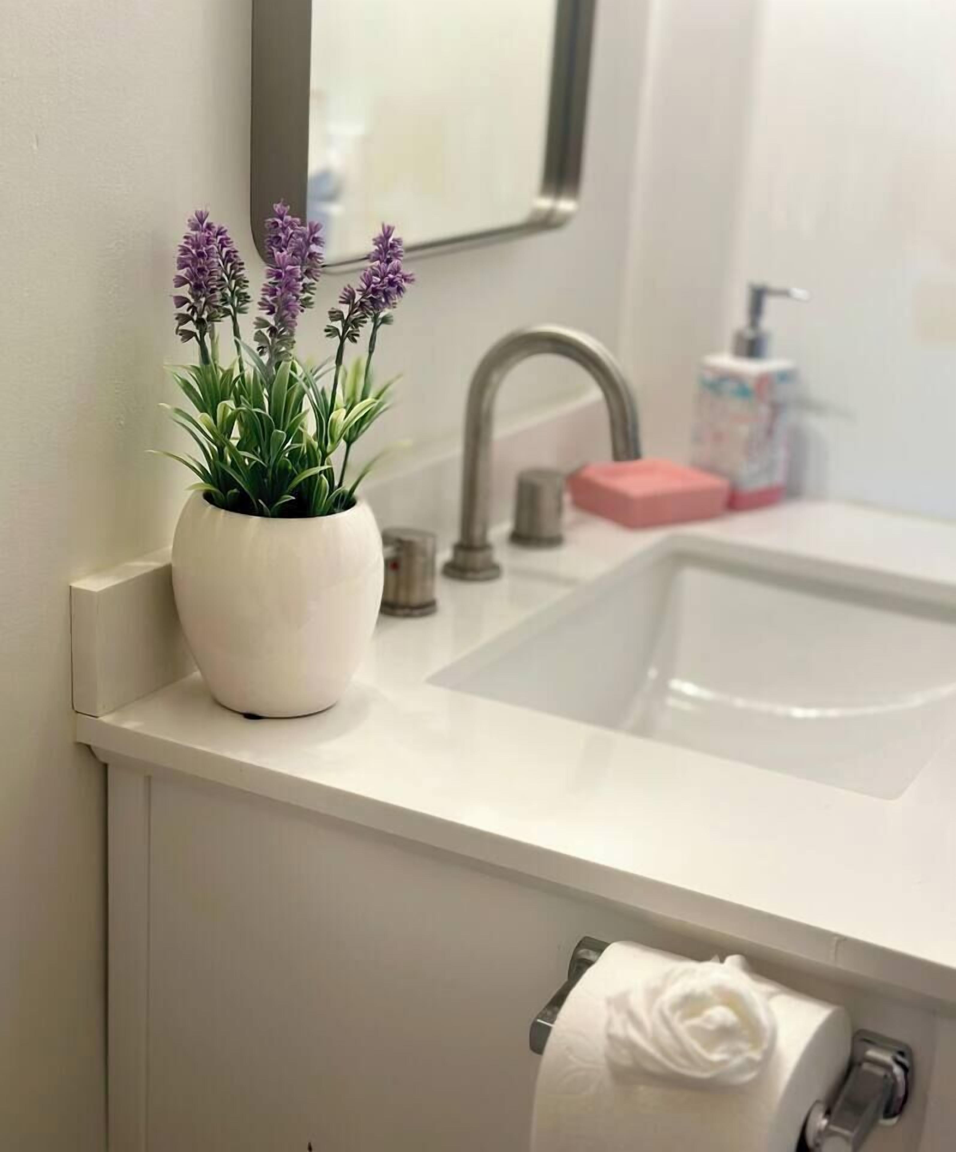 Ein Badezimmer mit Waschbecken, Spiegel, Topfpflanze und Handtuch.