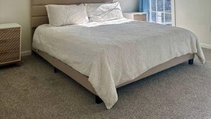 A bedroom with a bed, a ceiling fan, a nightstand, and a window with curtains. - Summerville’s Charm House (Summerville)