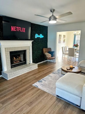 Een moderne woonkamer met een open haard, een flatscreen televisie, een plafondventilator en een gezellige zithoek.