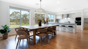 A modern kitchen with a wooden island, bar stools, and large windows offering a view of the outdoors. - Misty Ponds, Countryside at Berrima (Berrima)