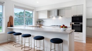A modern kitchen with a large island, bar stools, a herringbone backsplash, and a view of trees through the window. - Misty Ponds, Countryside at Berrima (Berrima)