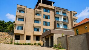 A multi-story building with balconies, a stone facade, and a paved entrance area. - KIGALI GOLDEN VILLA RESORTS WITH POOL (Kigali)