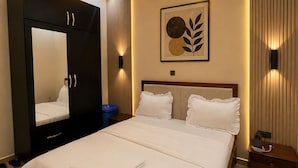 A neatly made bed with a white comforter and pillows, a large mirror, and a framed artwork on the wall. - KIGALI GOLDEN VILLA RESORTS WITH POOL (Kigali)