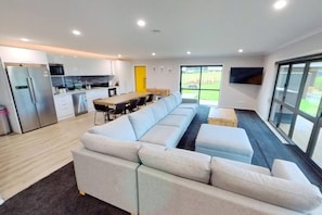 Ein modernes Wohnzimmer mit einer Couch, einem Esstisch mit Stühlen, einer Küchenzeile und einem großen Fenster.