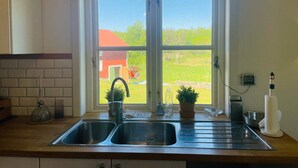 A kitchen with a double sink, a window with a view of a red barn and green field, and various kitchen items on the counter. - 4 Star Holiday Home in Ellos (Ellos)