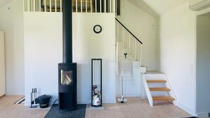 A modern interior with a black wood-burning stove, a white staircase, and a clock on the wall. - 4 Star Holiday Home in Ellos (Ellos)