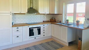 A kitchen with white cabinets, a wooden countertop, a stainless steel range hood, and a window with a view of a red building. - 4 Star Holiday Home in Ellos (Ellos)