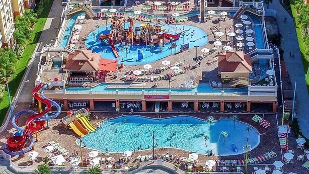 Ein Hotel mit großem Pool, Wasserrutschen und Strandbereich mit Liegestühlen.