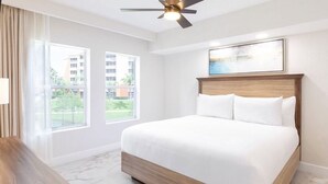 Ein Schlafzimmer mit einem großen Bett, einem Deckenventilator und einem Fenster mit Blick auf Gebäude.