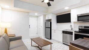 A modern kitchen with white cabinets, stainless steel appliances, and a flat-screen TV mounted above the oven. - Disney Area Resort Escape! (Kissimmee)