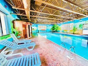 An indoor swimming pool with clear water, surrounded by lounge chairs and a tiled floor.