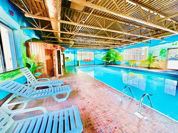 Una piscina interior con agua cristalina, rodeada de sillas de descanso y un suelo de baldosas.