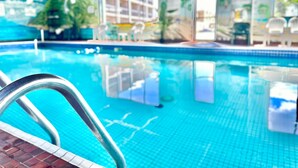 Une piscine intérieure à l’eau d’un bleu limpide, avec un escalier métallique et un sol carrelé.
