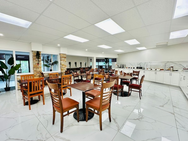 A spacious dining area with multiple tables and chairs, a kitchen area with modern appliances, and large windows allowing natural light.