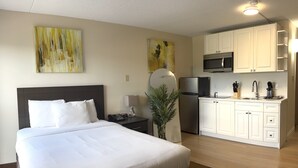 Hotellihuone, jossa on sänky, yöpöytä, työpöytä, jääkaappi, mikroaaltouuni ja pieni keittotila.