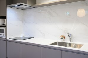 Una cocina moderna con salpicadero de mármol blanco, pileta de acero inoxidable y horno empotrado.