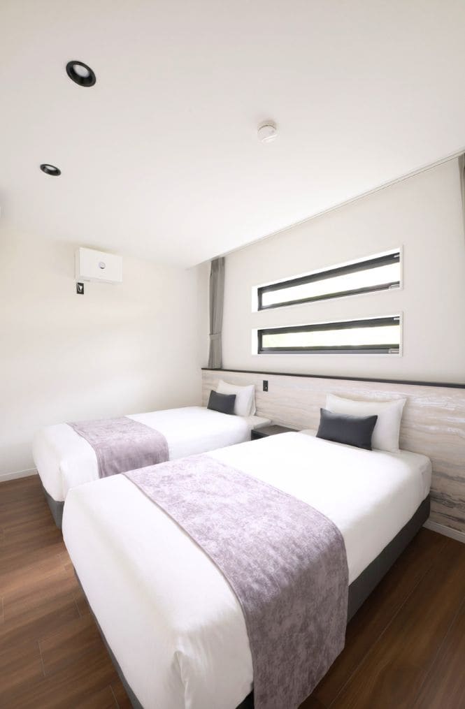 A modern hotel room with two beds, a large mirror, and a ceiling light.