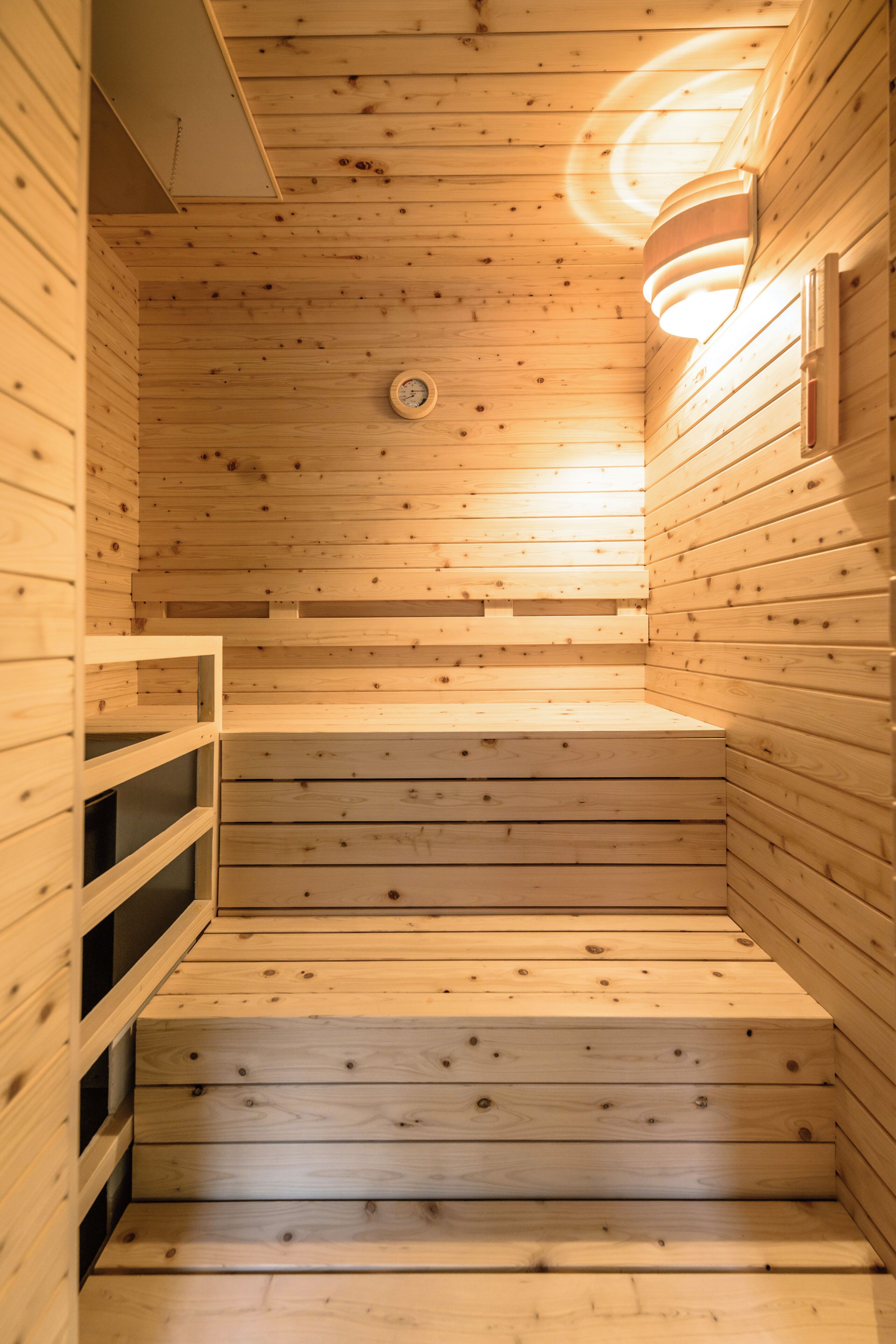 Un sauna en bois doté d’un plafond incliné et d’un luminaire fixé au mur.