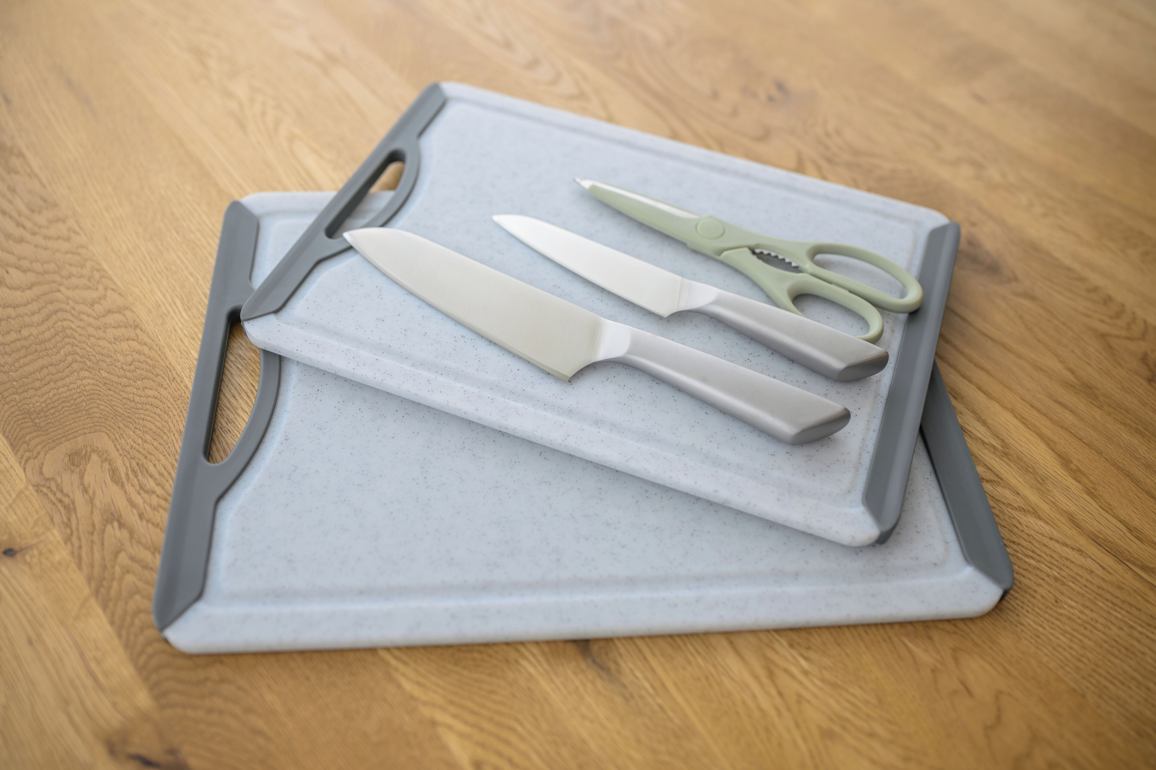 A cutting board with a knife, scissors, and a peeler on a wooden surface.