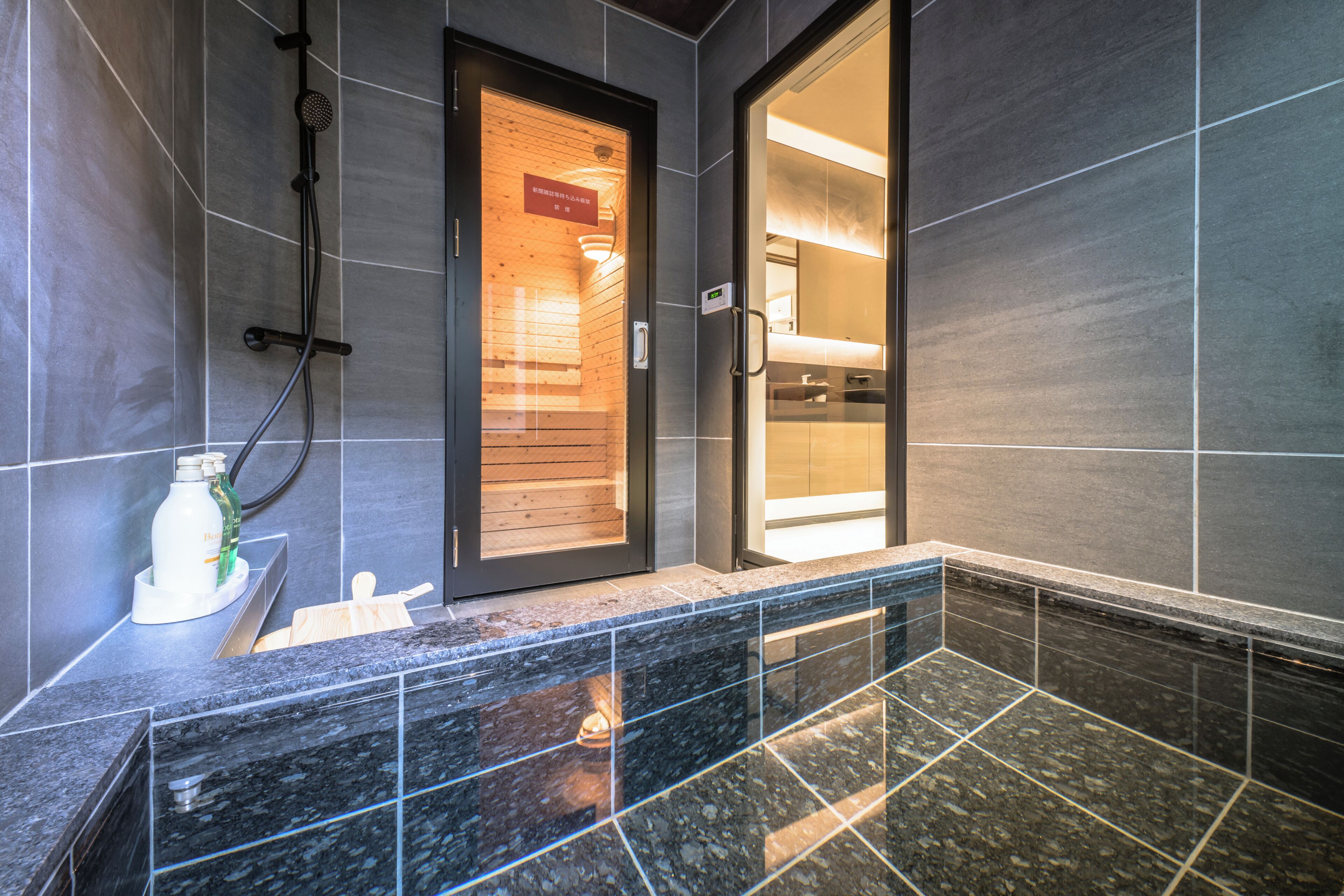 Un baño moderno con baldosas oscuras, zona de ducha y tocador con espejo.