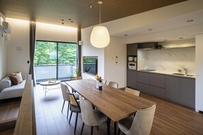 Una cocina moderna con encimera de mármol, un comedor con mesa y sillas de madera, y una sala de estar con sofá y televisor.