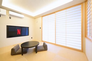 A room with tatami flooring, a low table, two cushions, a television with a red 'N' logo, and sliding shoji doors. - Stagione Hakone Sengokuhara Monte (Ashigarashimo gun Hakone-machi)
