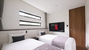 Habitación de hotel con dos camas, un televisor montado en la pared y una puerta de madera.