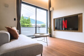Una sala de estar moderna con un sofá, una mesita redonda, una planta en maceta y un ventanal con vistas a la vegetación y montañas.