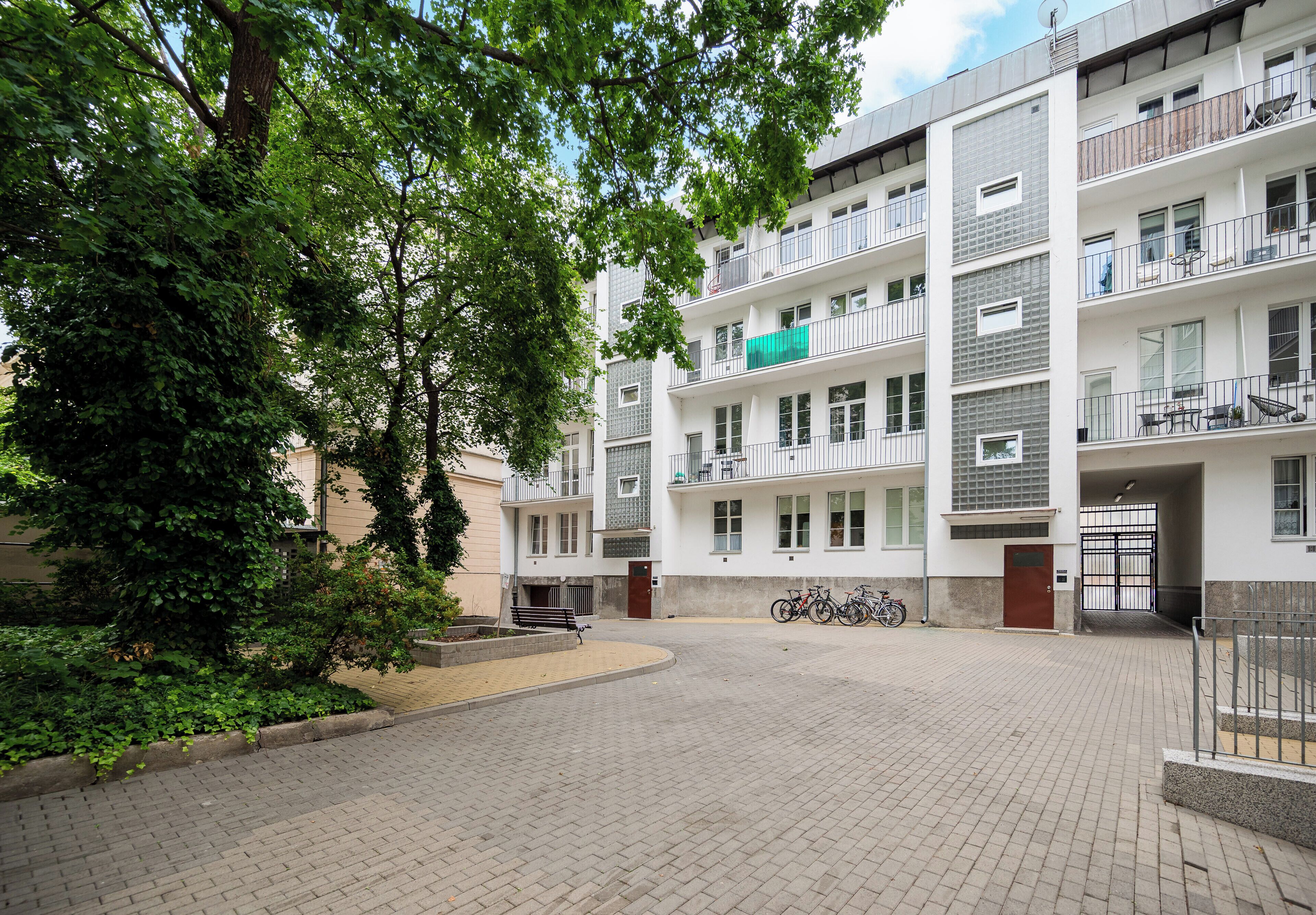 Un immeuble résidentiel à plusieurs étages, doté de balcons, d’une cour pavée et de vélos garés à l’extérieur.