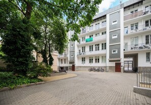 Kerrostalo, jossa on useita kerroksia, parvekkeet, kivetty sisäpiha ja pyöriä parkkeerattuna ulkona.