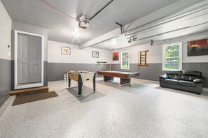 A room with a pool table, foosball table, and a sofa.