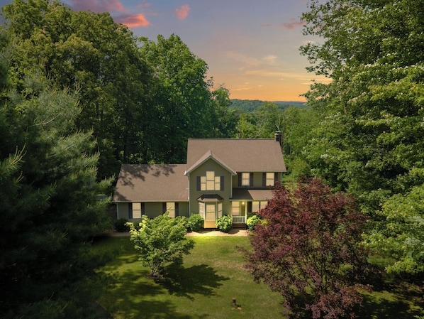 A two-story house with a front yard, surrounded by trees.
