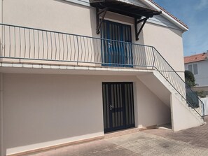 Ein zweistöckiges Gebäude mit Balkon, einer schwarzen Tür und einer Treppe, die zu der oberen Etage führt.